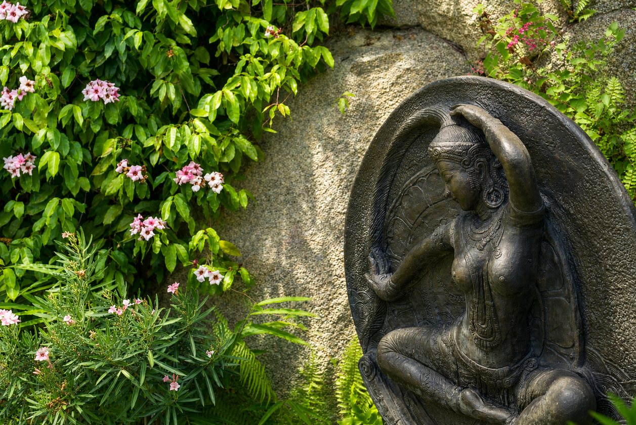 Carved stone deity sculpture among flowering plants
